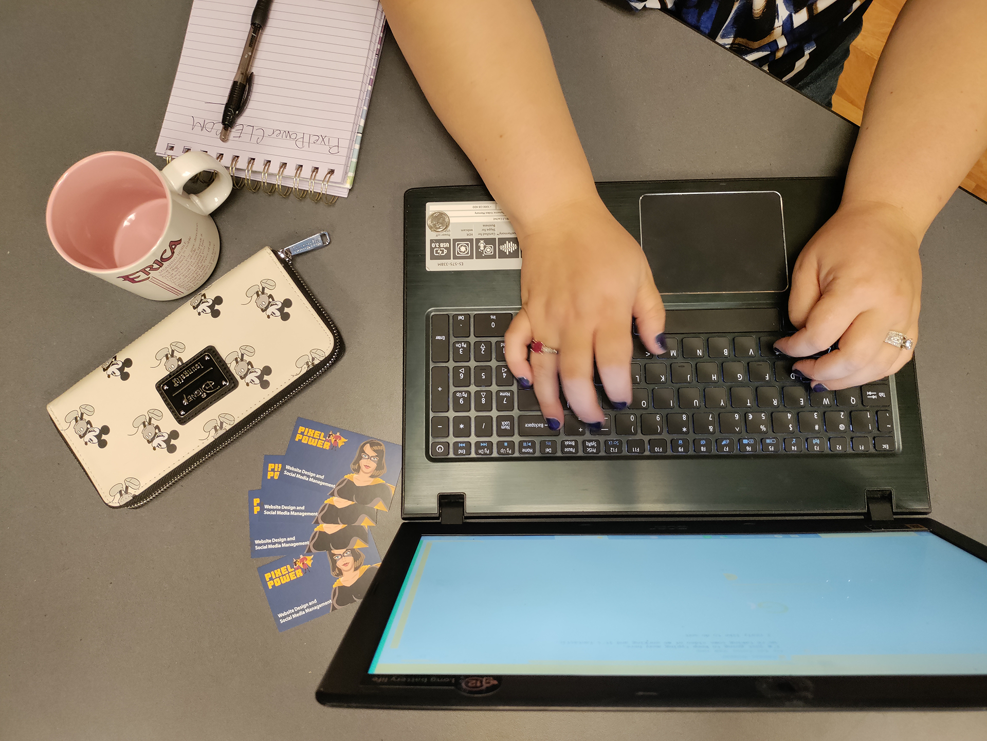 Ladies hands typing on a computer with business cards, mug, and wallet nearby